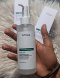 Hand holding a skincare product labeled 'anua' with a blurred background