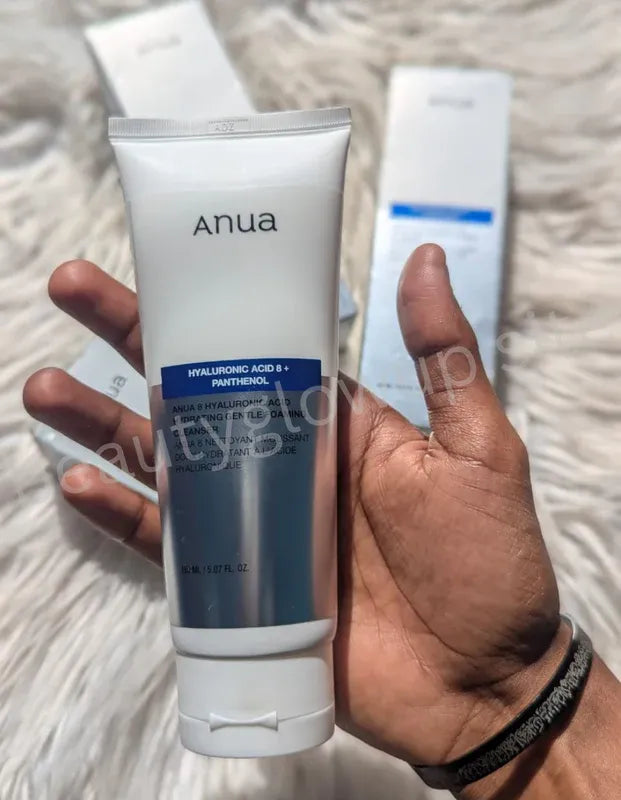 Hand holding a tube of 'anua' skincare product on a textured surface