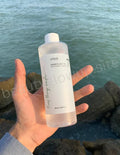 Hand holding a bottle of skincare product with a scenic background