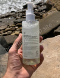 Hand holding a bottle of skincare product with a rocky beach background