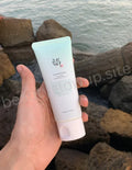 Hand holding a skincare product with a coastal background