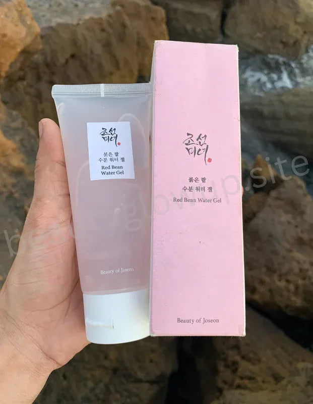 Hand holding a tube and box of Beauty of Joseon Red Bean Water Gel against a stone background
