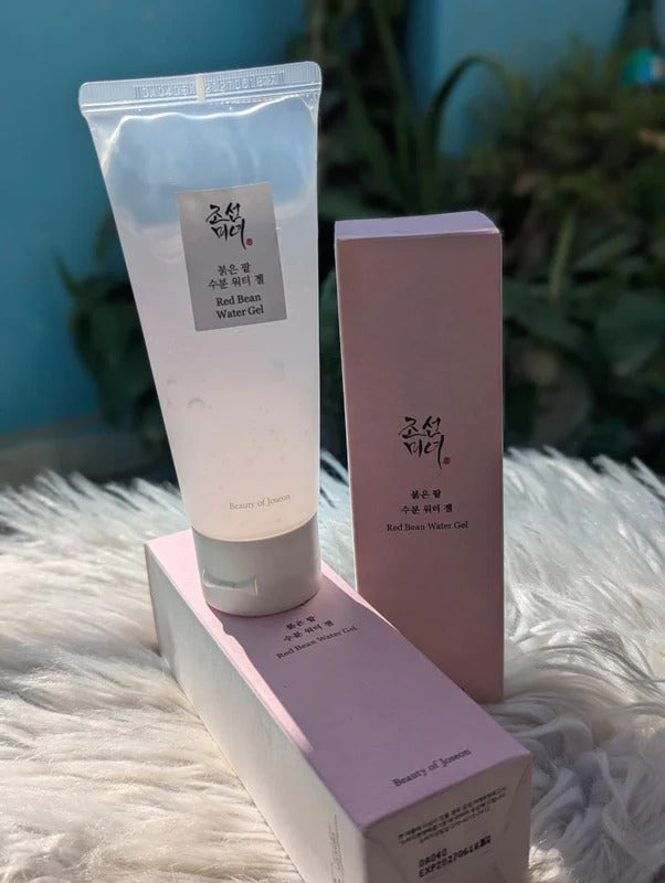 Two skincare products with pink packaging on a textured surface with a blurred green plant background.