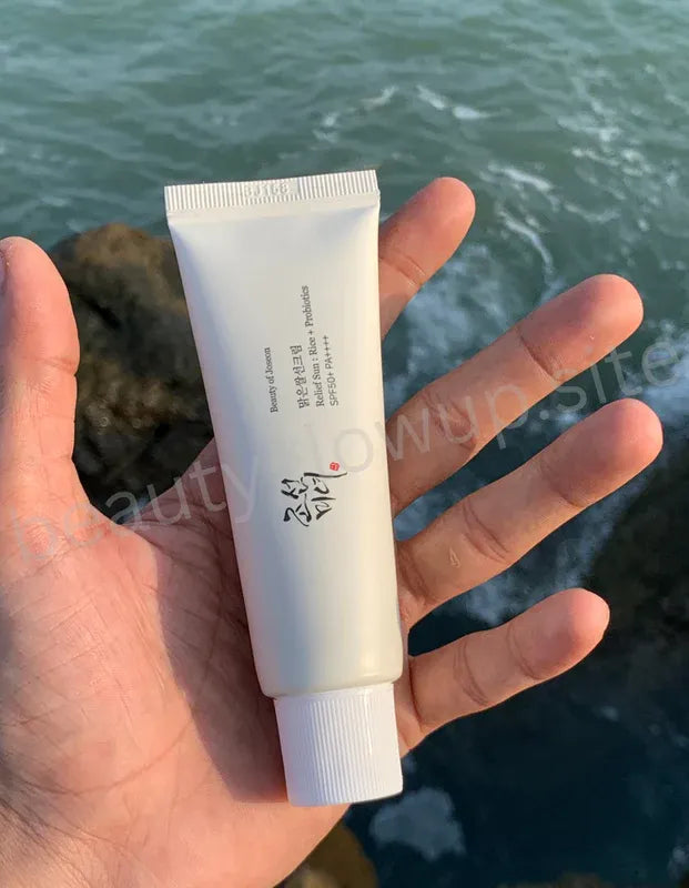 Hand holding a tube of beauty of joeson and a box with a brand logo against a blurred natural background