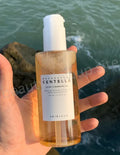 Bottle of Skintouch Centella Light Cleansing Oil held by a hand with ocean background