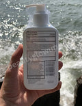 Hand holding a bottle of lotion with a blurred water background