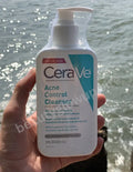 CeraVe Acne Control Cleanser bottle held in front of a water background