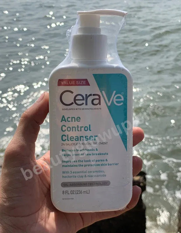 CeraVe Acne Control Cleanser bottle held in front of a water background