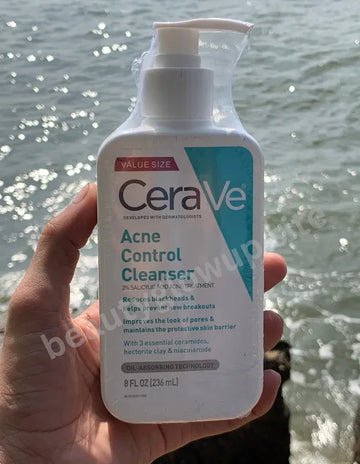 CeraVe Acne Control Cleanser bottle held in front of a water background