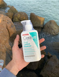 CeraVe Acne Control Cleanser held by a hand with a rocky beach background