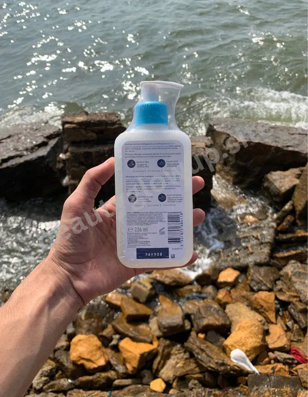 Hand holding a bottle of hand sanitizer with a scenic background of water and rocks.