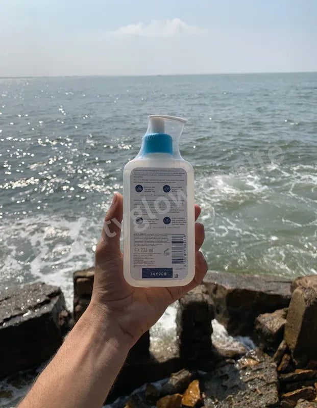 Hand holding a bottle of lotion with a beach background