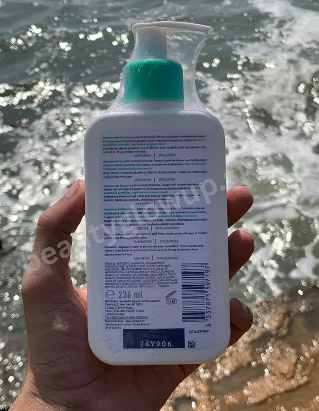 Hand holding a bottle of hand sanitizer with a blurred water background