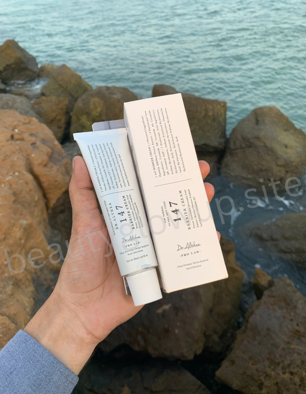 "Hand holding luxury skincare products with rocks and water in the background, highlighting natural ingredients."