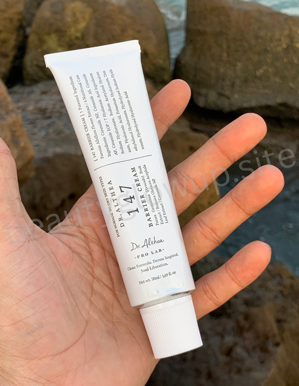 "Hand holding luxury skincare products with rocks and water in the background, highlighting natural ingredients."