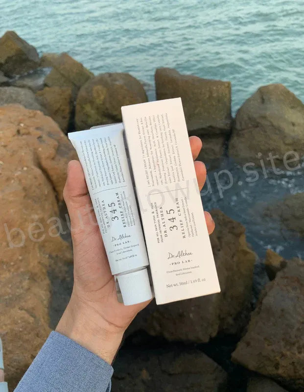 Hand holding skincare products with a scenic background of rocks and water.