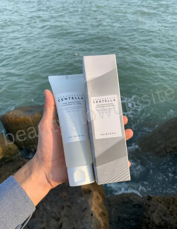 Hand holding a tube and box of Centella Asiatica skincare product by Benton against a natural background.