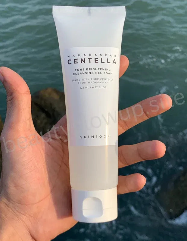 Hand holding a tube and box of Centella Asiatica skincare product by Benton against a natural background.