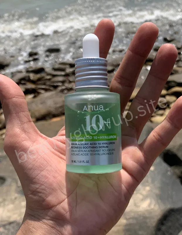 Hand holding a bottle of Anua 10+ serum with a beach background