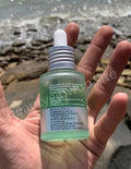 Hand holding a skincare serum bottle with a blurred natural background