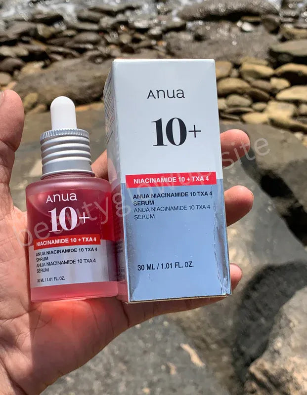 Anua 10+ skincare serum bottle and box held in a hand with a rocky background