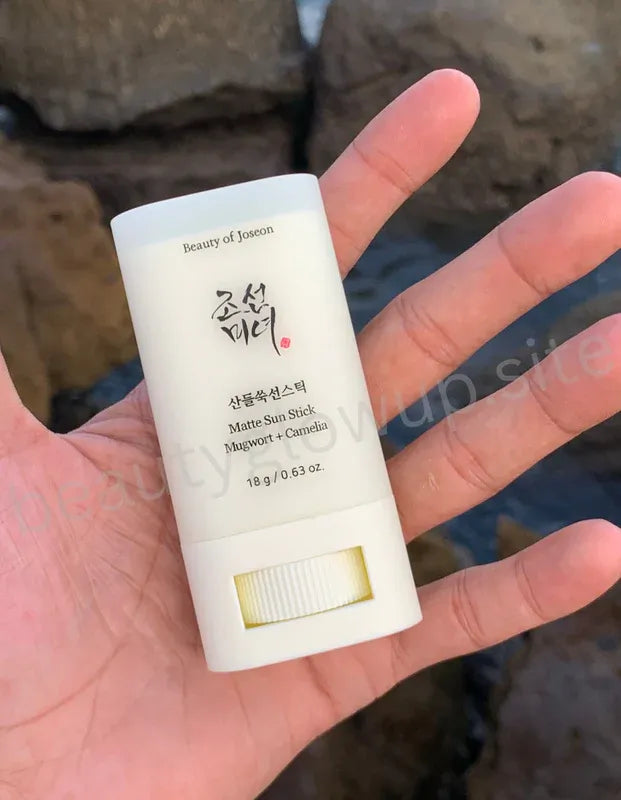 Hand holding a beauty of joeson stick and its packaging with a blurred natural background