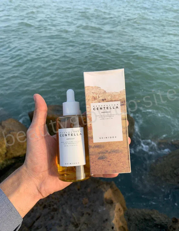Hand holding a bottle and box of Centella Asiatica by Aromatica against a water background