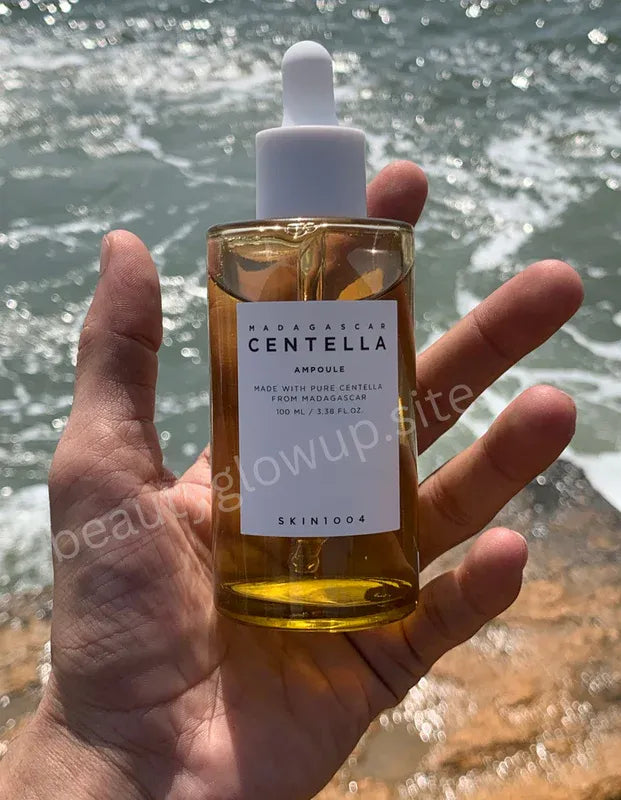 Hand holding a bottle and box of Centella Asiatica by Aromatica against a water background