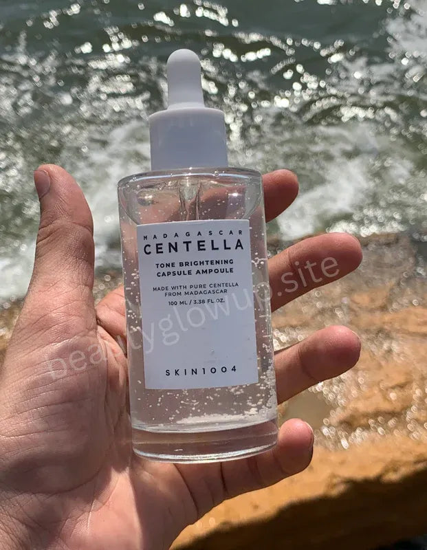 Hand holding a skincare bottle labeled 'SKIN1004' with a natural background