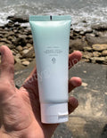 Hand holding a light blue skincare product tube with a natural background