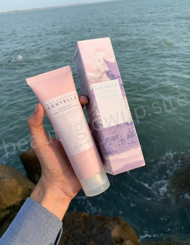 Hand holding a pink skincare product and its packaging by a body of water