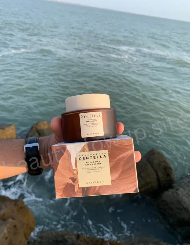 Hand holding a Skinceuticals Centella product with ocean view
