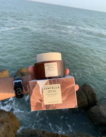 Hand holding a Skinceuticals Centella product with ocean view