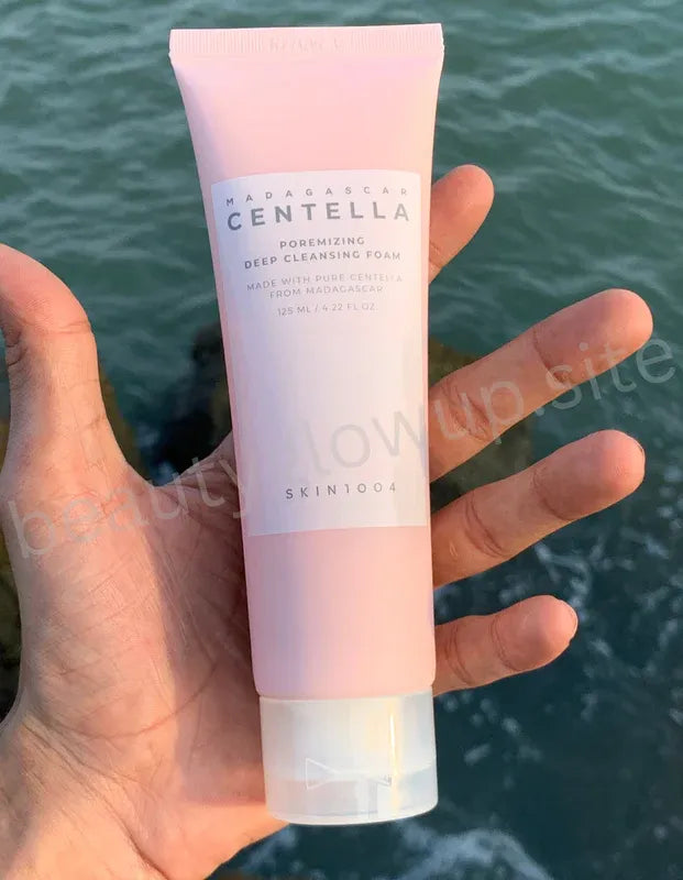 Hand holding a pink tube of Centella Cleansing Foam against a blurred natural background