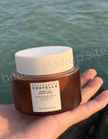 Jar of skincare cream held by a hand with a blurred natural background