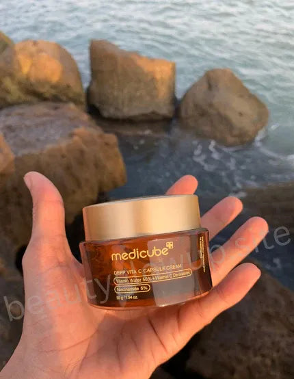 Hand holding a jar of Medicube skincare product with a beach background